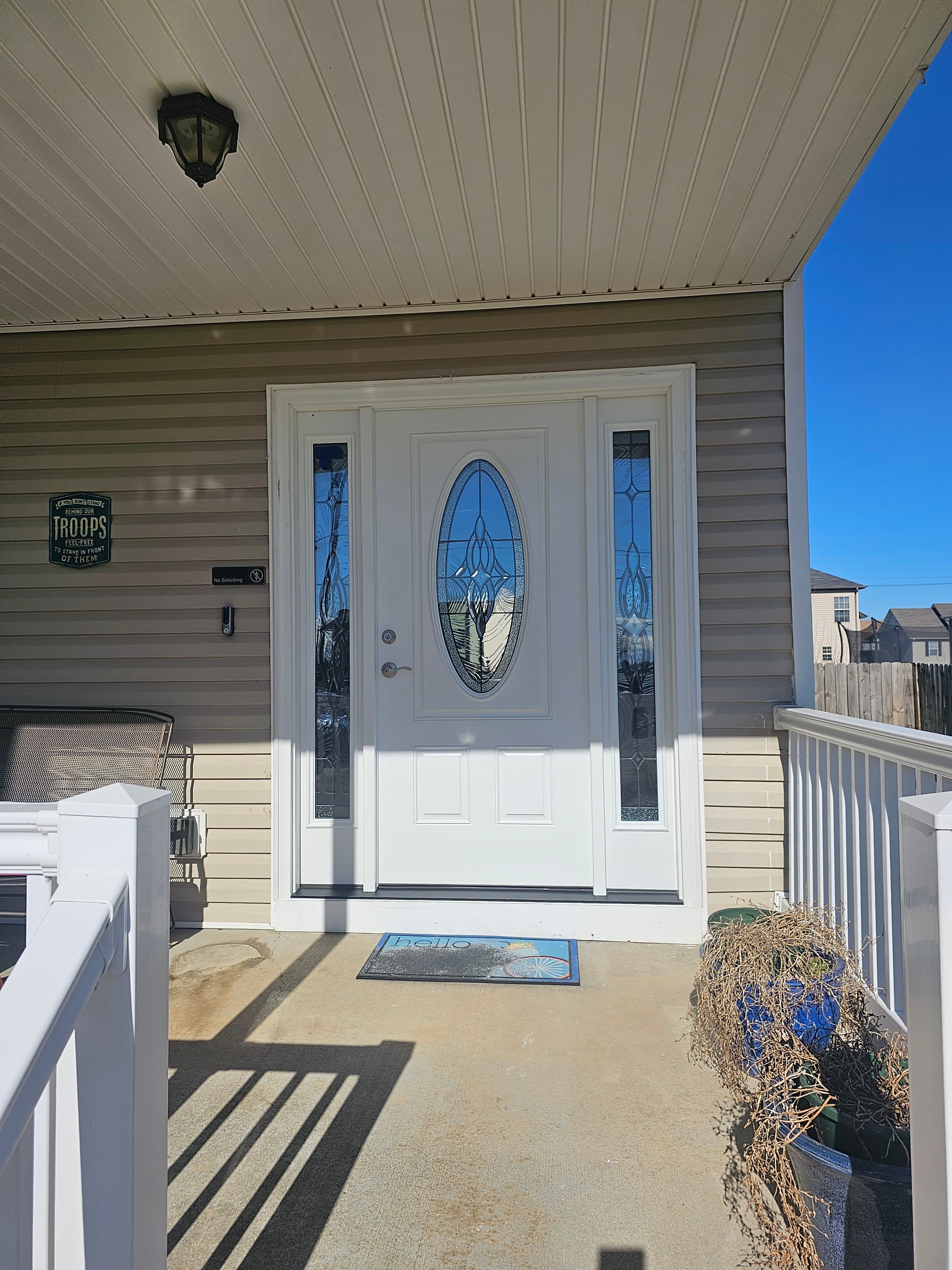 White front door with oval decorative glass and sidelights on a porch with tan siding.