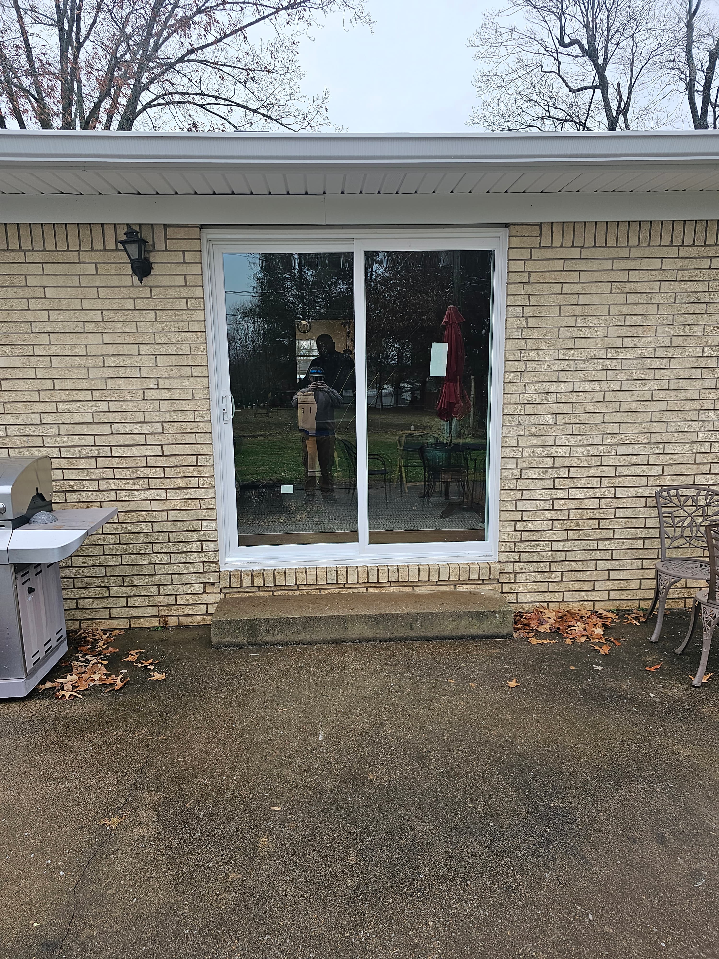 White sliding glass door set in a tan brick wall above a concrete patio.