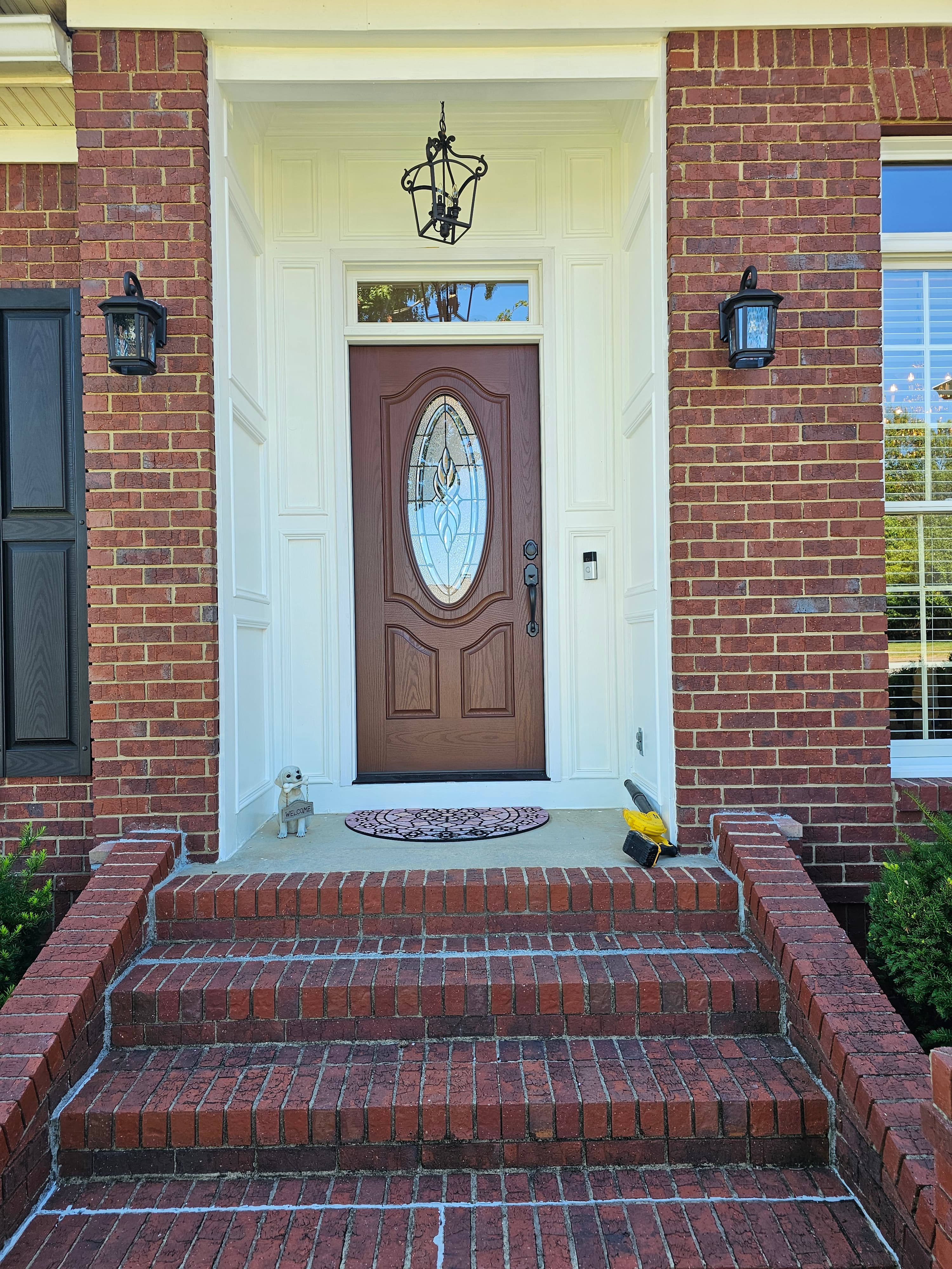 Brown front door with oval glass pane, white trim, and wide red brick steps.